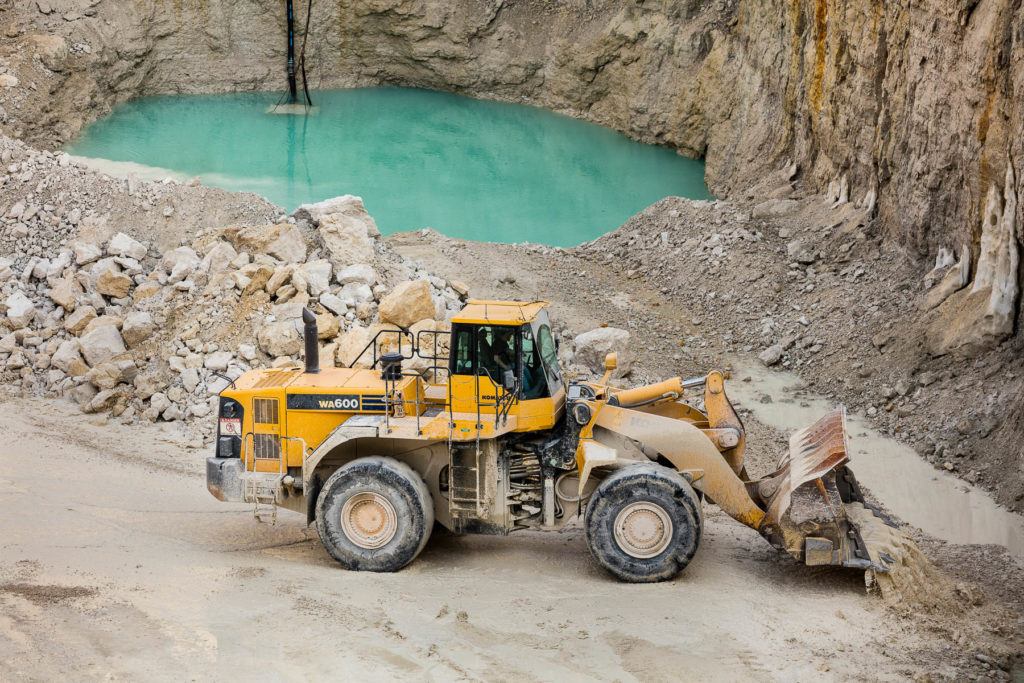 Industrial photography of a surface mine with an earthmoving machine in front of a deep aqua lake in Iowa